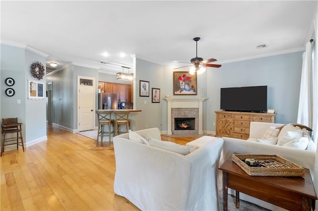 living room with a fireplace, ornamental molding, ceiling fan, and light wood-type flooring