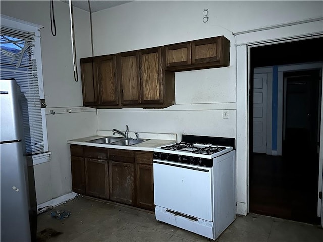 kitchen with dark brown cabinets, sink, stainless steel refrigerator, and gas range gas stove