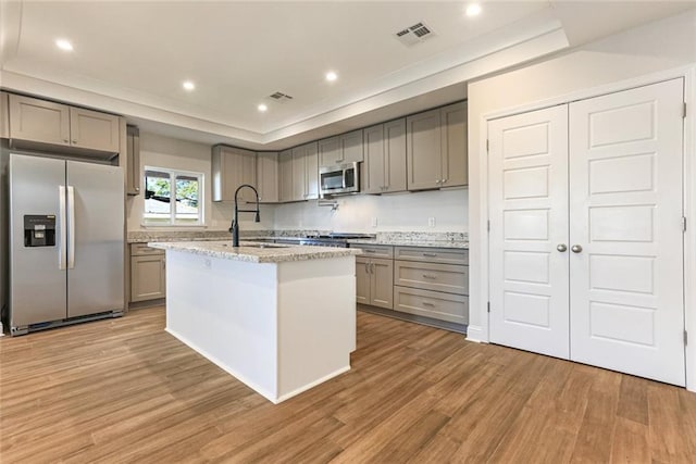 kitchen with light hardwood / wood-style flooring, light stone countertops, an island with sink, and appliances with stainless steel finishes