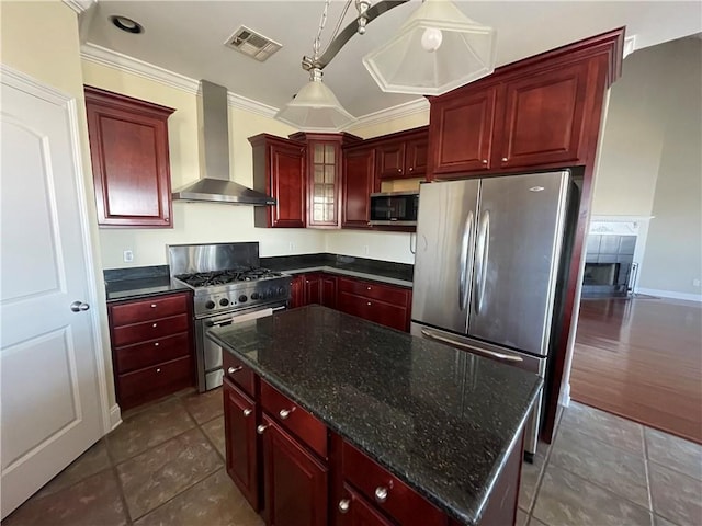 kitchen featuring pendant lighting, dark stone countertops, a center island, stainless steel appliances, and wall chimney exhaust hood