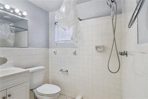 bathroom featuring tile walls, vanity, toilet, and walk in shower