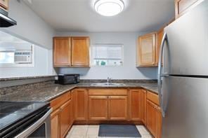 kitchen featuring sink, dark stone countertops, stainless steel refrigerator, and light tile patterned floors