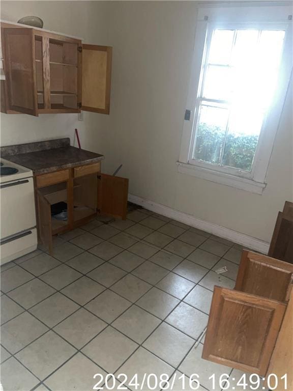 kitchen with white electric stove, baseboards, dark countertops, brown cabinets, and light tile patterned flooring