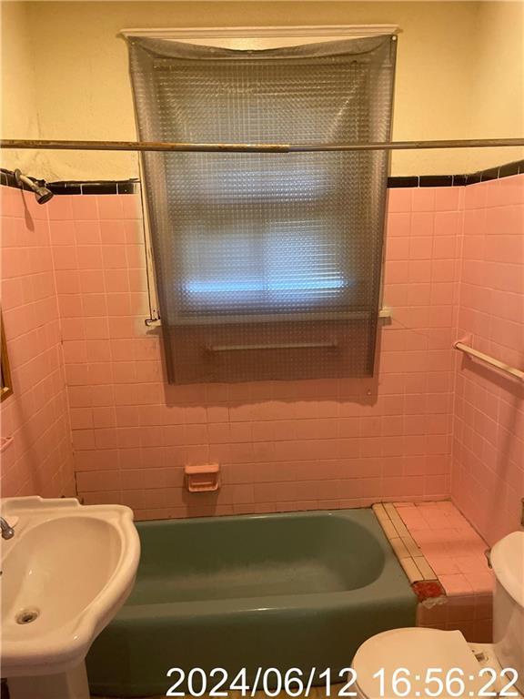 full bath featuring toilet, a washtub, tile walls, and a sink