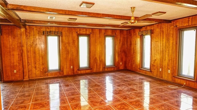 tiled spare room with ceiling fan, wooden walls, beam ceiling, and a textured ceiling