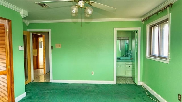 unfurnished bedroom featuring ornamental molding, ensuite bathroom, ceiling fan, and dark colored carpet