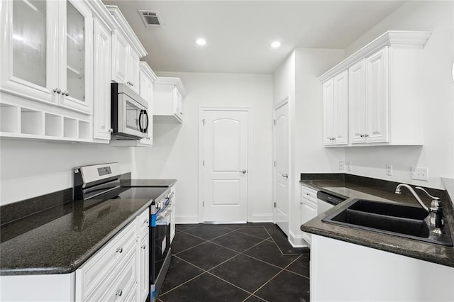 kitchen with sink, appliances with stainless steel finishes, dark stone countertops, white cabinets, and dark tile patterned flooring