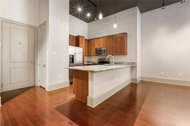 kitchen featuring brown cabinets, a high ceiling, appliances with stainless steel finishes, a peninsula, and dark wood-style flooring