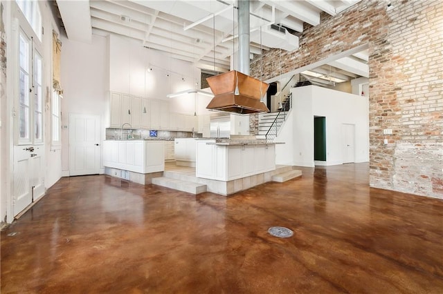 kitchen with concrete flooring, custom range hood, white cabinets, and a high ceiling