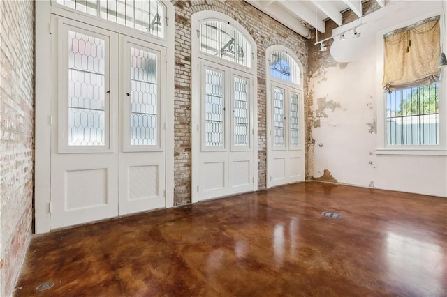 entryway featuring a high ceiling, beamed ceiling, and brick wall