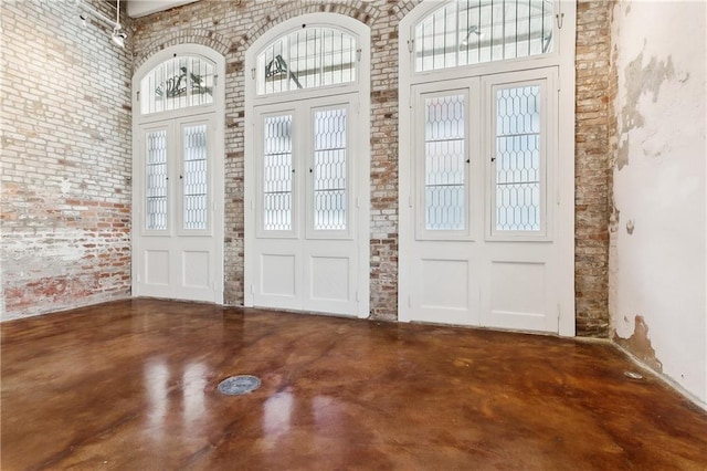 foyer with a high ceiling, concrete flooring, brick wall, and french doors