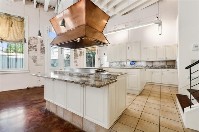 kitchen featuring a kitchen island, island range hood, white cabinets, dark stone counters, and a high ceiling