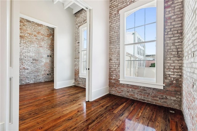 unfurnished bedroom featuring dark wood-type flooring, a towering ceiling, and brick wall