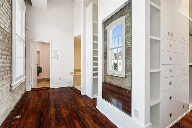 corridor with a towering ceiling, brick wall, and dark hardwood / wood-style floors