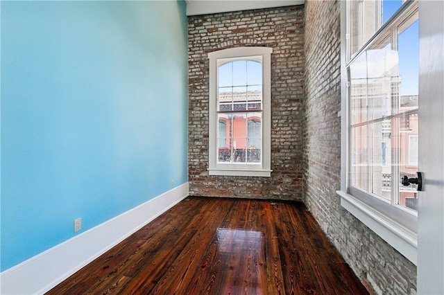 empty room with dark wood-type flooring, plenty of natural light, and brick wall