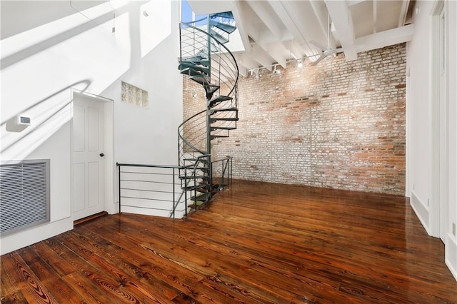 unfurnished living room with dark hardwood / wood-style flooring, a towering ceiling, beam ceiling, and brick wall