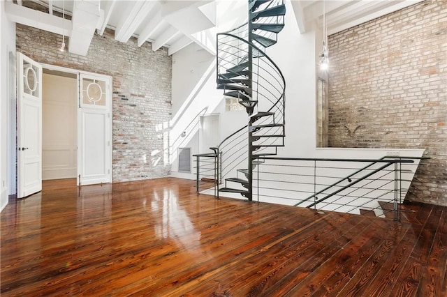 stairs with a towering ceiling, brick wall, and wood-type flooring