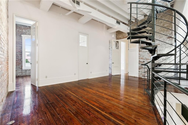 interior space featuring beam ceiling, wood-type flooring, ceiling fan, and brick wall