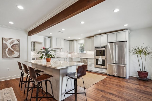 kitchen featuring appliances with stainless steel finishes, a breakfast bar, white cabinets, a center island, and beam ceiling