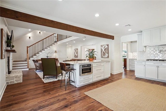 kitchen with dark hardwood / wood-style floors, an island with sink, white cabinets, a kitchen bar, and stainless steel oven