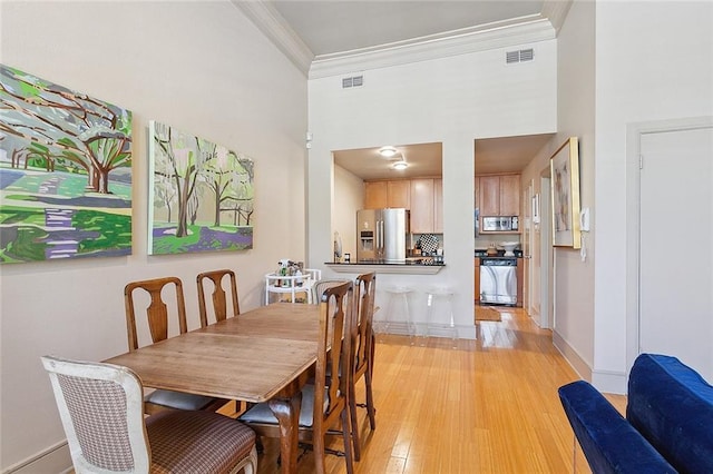 dining space featuring a high ceiling, ornamental molding, sink, and light hardwood / wood-style floors