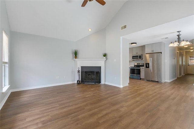 unfurnished living room with high vaulted ceiling, ceiling fan with notable chandelier, and light hardwood / wood-style floors