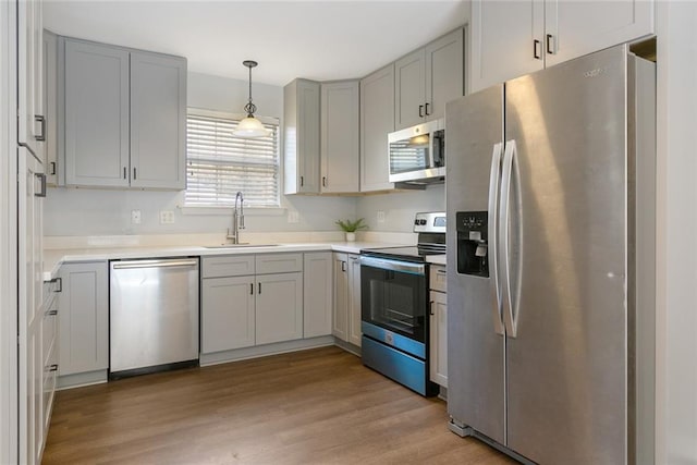 kitchen with gray cabinets, appliances with stainless steel finishes, sink, hanging light fixtures, and light hardwood / wood-style flooring