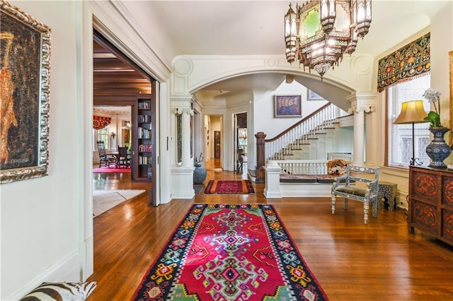 foyer featuring hardwood / wood-style flooring, an inviting chandelier, and decorative columns