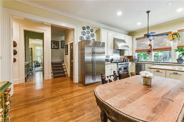 kitchen featuring white cabinetry, crown molding, light wood-type flooring, high quality appliances, and wall chimney range hood