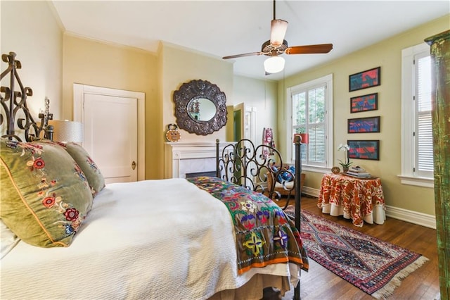 bedroom with crown molding, wood-type flooring, a tile fireplace, and ceiling fan