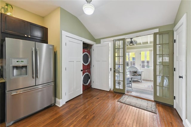 kitchen featuring stainless steel fridge, dark brown cabinets, stacked washer / dryer, dark hardwood / wood-style flooring, and vaulted ceiling