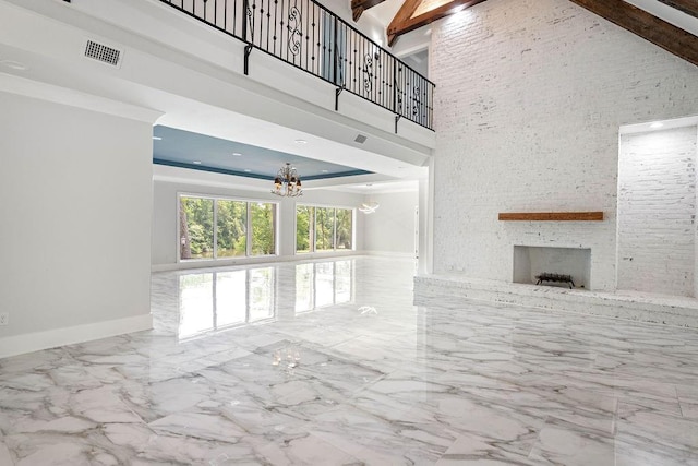 unfurnished living room with beamed ceiling, a towering ceiling, a notable chandelier, and a fireplace