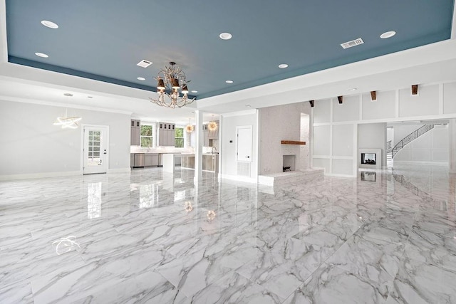 unfurnished living room featuring a large fireplace, a raised ceiling, and a chandelier