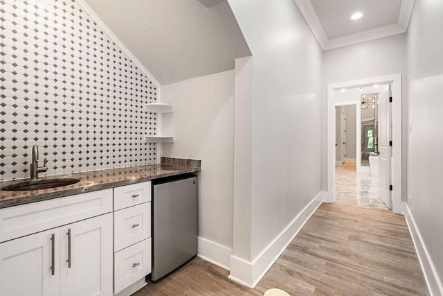 kitchen featuring white cabinetry, sink, dark stone countertops, ornamental molding, and light hardwood / wood-style flooring