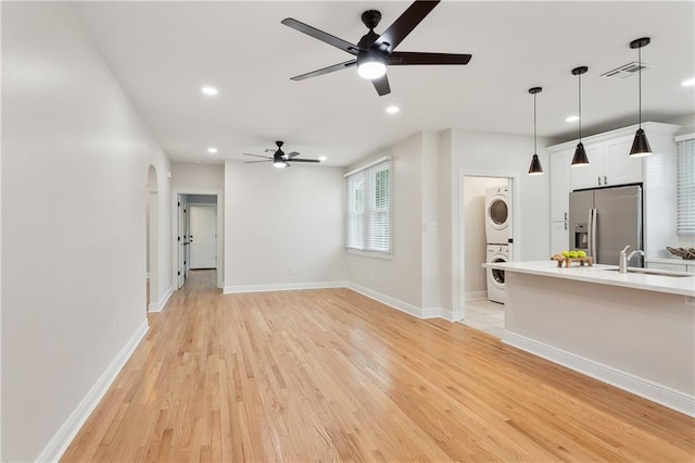 unfurnished living room featuring ceiling fan, stacked washer / drying machine, light hardwood / wood-style floors, and sink