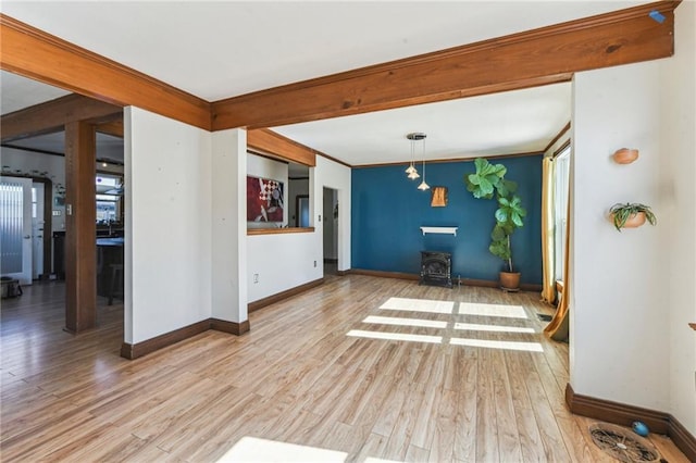 interior space with beamed ceiling, ornamental molding, a wood stove, and light wood-type flooring