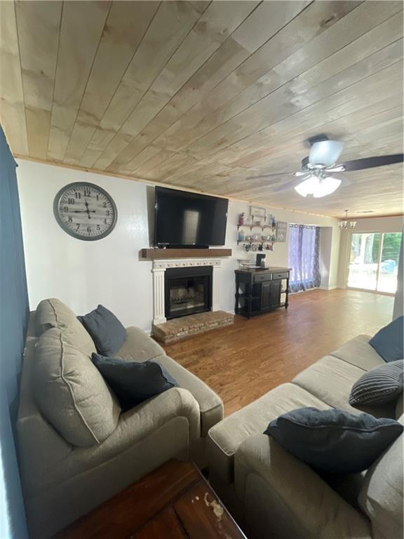 living room featuring ceiling fan, wood-type flooring, a fireplace, and wooden ceiling