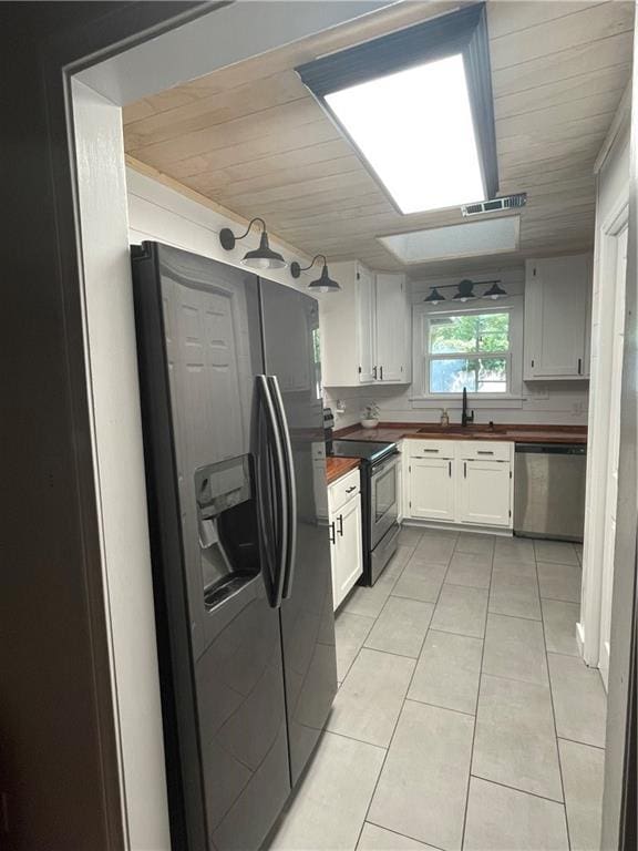 kitchen with appliances with stainless steel finishes, sink, light tile patterned floors, and wooden counters