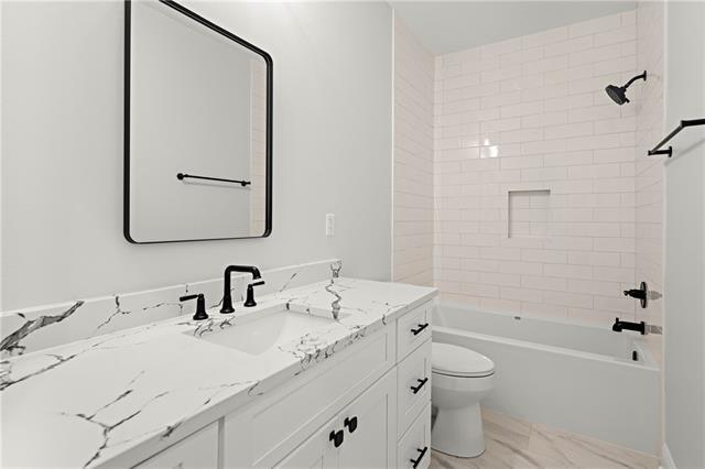 full bathroom featuring vanity, tiled shower / bath, and toilet