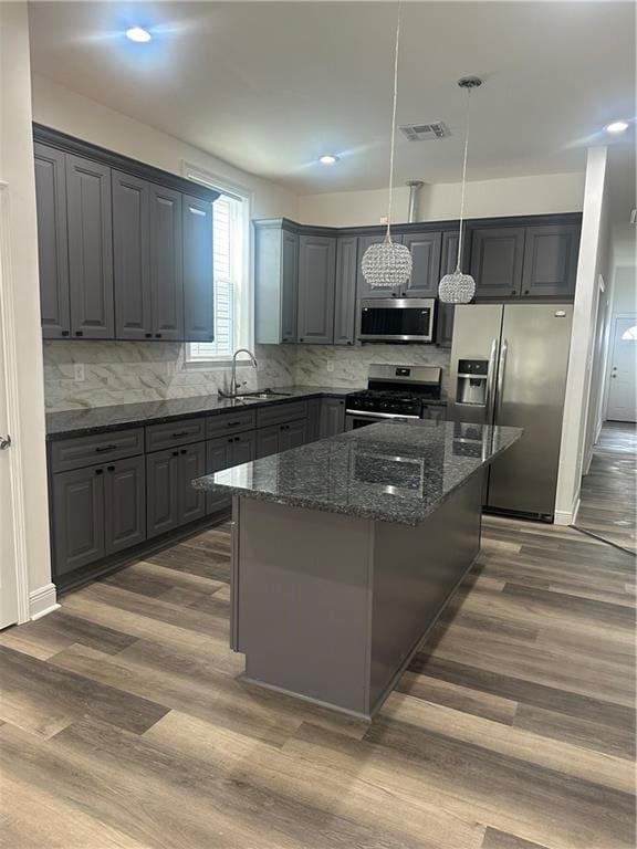 kitchen featuring sink, dark stone countertops, a kitchen island, pendant lighting, and stainless steel appliances