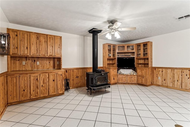 living room featuring wooden walls, ceiling fan, and a wood stove