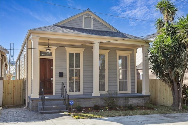 view of front facade featuring a porch, roof with shingles, and fence