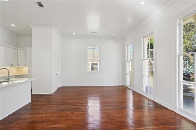 unfurnished living room with dark wood finished floors, visible vents, a healthy amount of sunlight, and ornamental molding