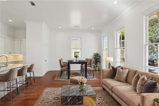 living area with a wealth of natural light, visible vents, dark wood-type flooring, and ornamental molding