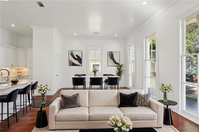 living area featuring dark wood-type flooring, visible vents, a wealth of natural light, and ornamental molding