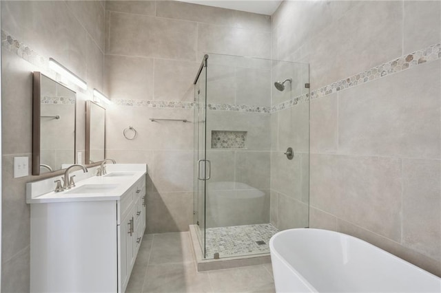 bathroom featuring a stall shower, a freestanding bath, tile patterned flooring, a sink, and tile walls