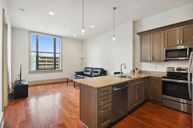 kitchen with decorative light fixtures, sink, light stone counters, kitchen peninsula, and stainless steel appliances