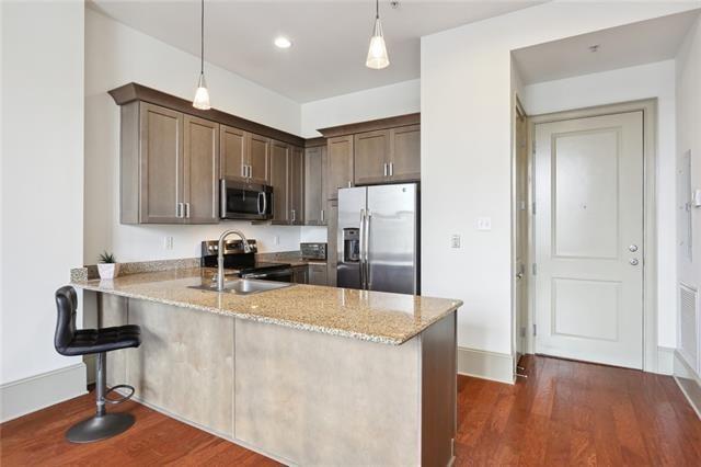 kitchen with stainless steel appliances, hanging light fixtures, light stone counters, and kitchen peninsula