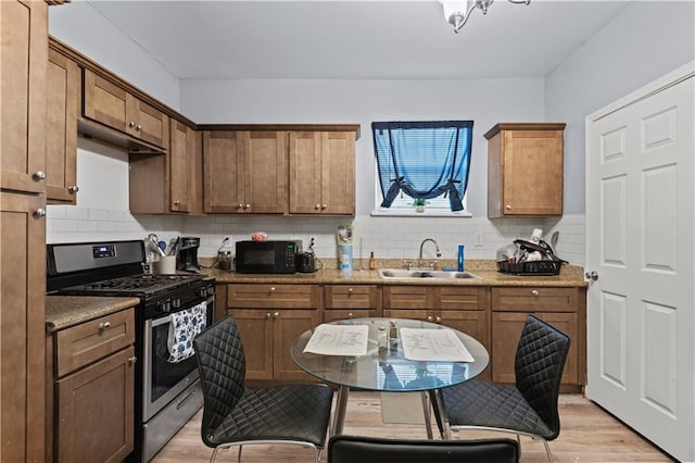 kitchen featuring sink, tasteful backsplash, light hardwood / wood-style floors, light stone countertops, and gas stove