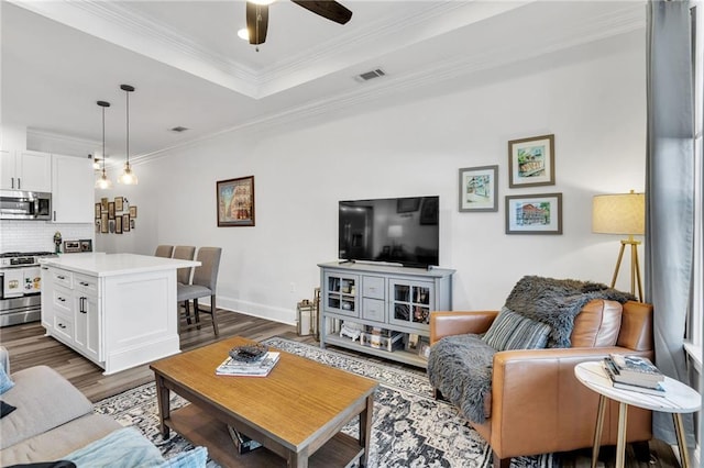 living area with dark wood-style floors, visible vents, a tray ceiling, ceiling fan, and ornamental molding
